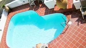 Una piscina con forma de corazón, con solárium alicatado y mobiliario exterior.