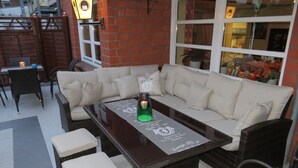 A cozy outdoor seating area with a wicker sofa, two cushioned chairs, and a glass-top table. - Hotel an der Hörn (Kiel)