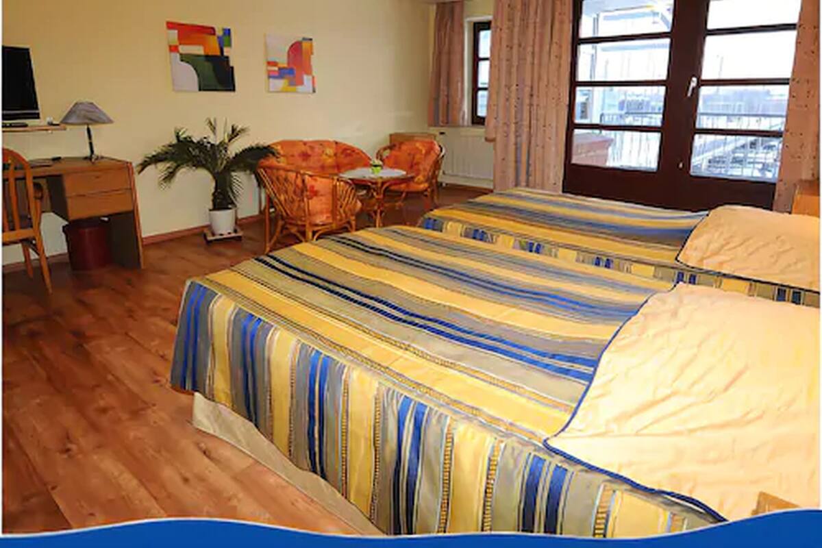 A hotel room with a large bed, a desk, a chair, a small table, and a potted plant.