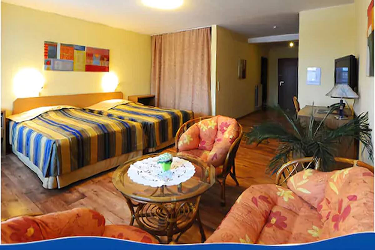 A hotel room with a bed, a chair, a small table with a doily, and a potted plant.