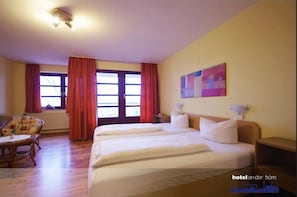 A hotel room with two beds, a sofa, a table, and a window with curtains. - Hotel an der Hörn (Kiel)