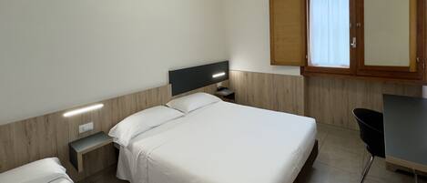 A hotel room with a bed, a TV, a small bedside table, a cabinet, and a window with curtains.