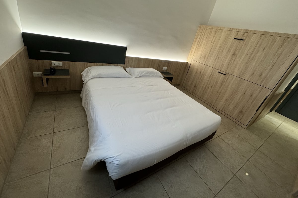 A modern bedroom with a large bed, wooden headboard, bedside tables, and a wardrobe.