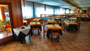 Uma sala de jantar ampla com várias mesas, cadeiras e plantas em vasos.