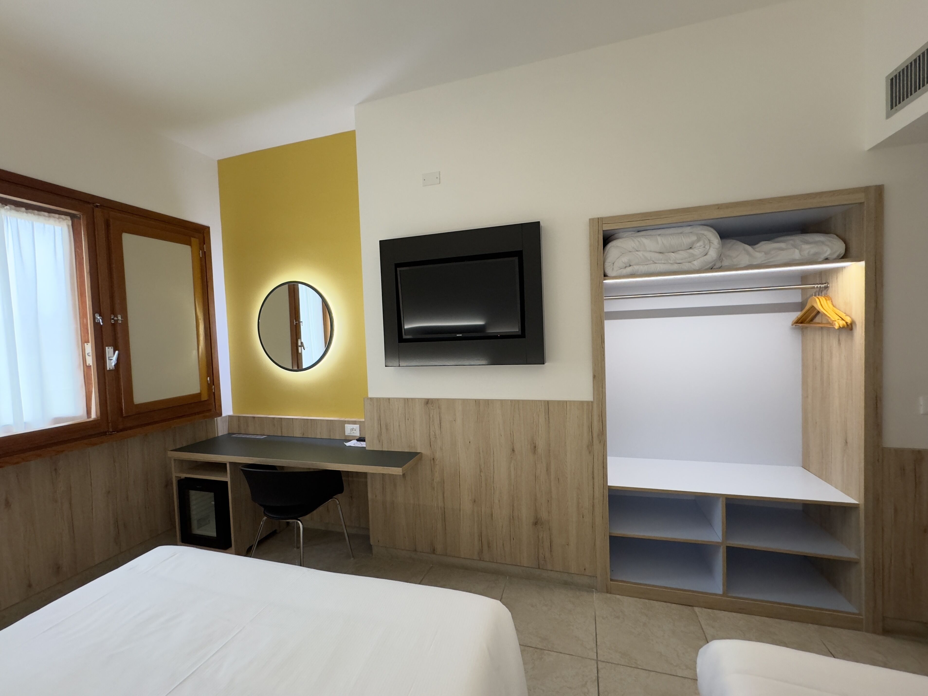 Una habitación de hotel con una cama, un escritorio, un televisor, un espejo y un armario.