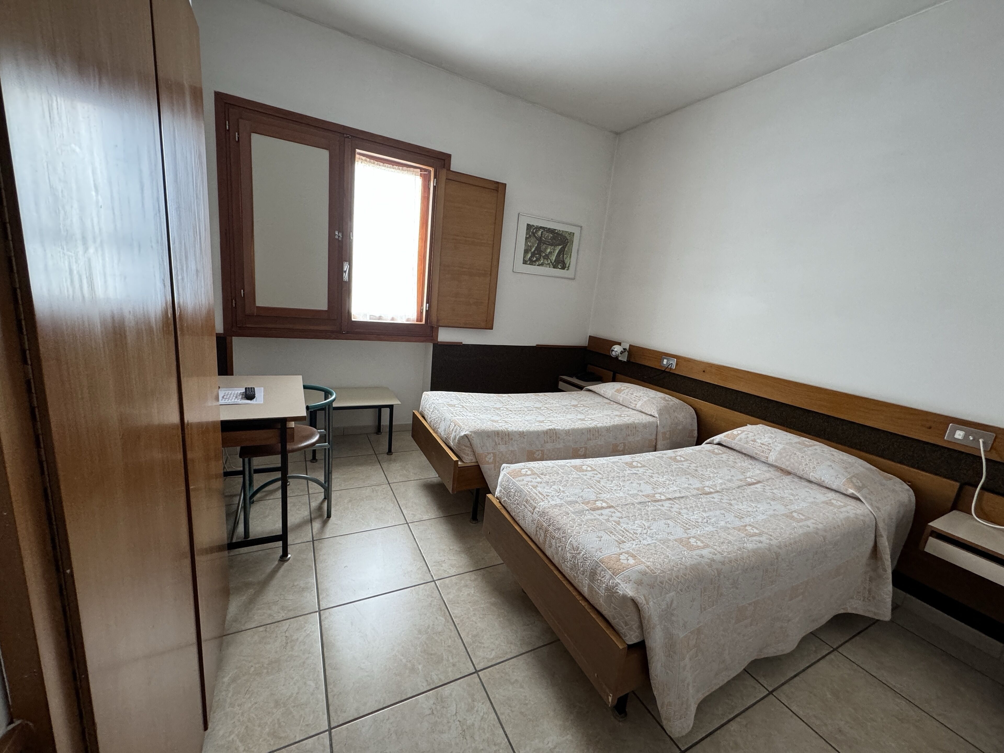 A small, clean room with two single beds, a desk, and a chair.