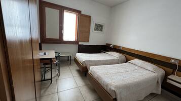 A small, clean room with two single beds, a desk, and a chair.