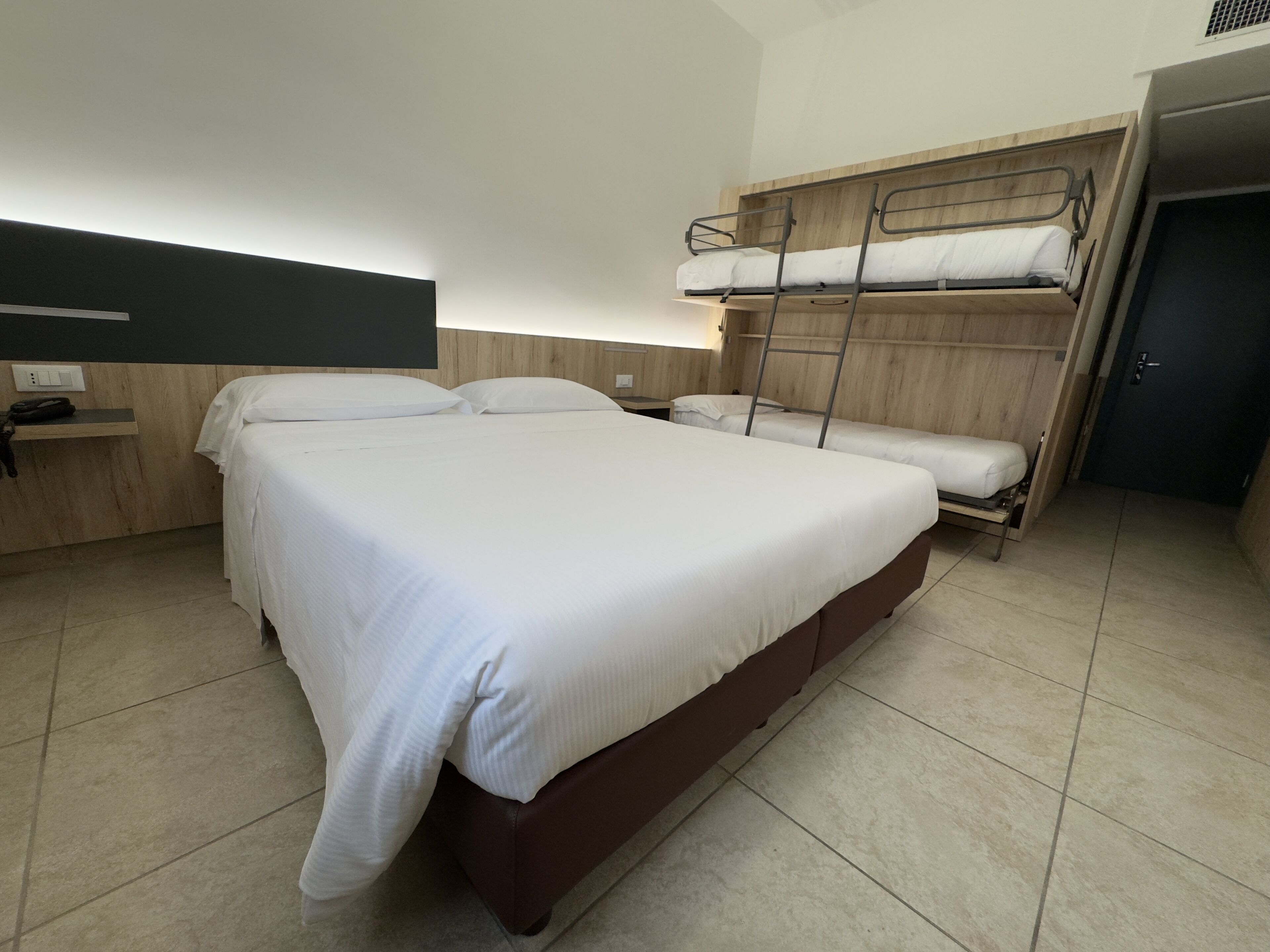 Ein Hotelzimmer mit einem großen Bett, einem Schlafkoje und einem Nachttisch, sowie einem an der Wand montierten Fernseher.