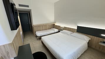 Une chambre d’hôtel avec deux lits simples, un bureau avec une chaise, un téléviseur à écran plat fixé au mur et une petite table.