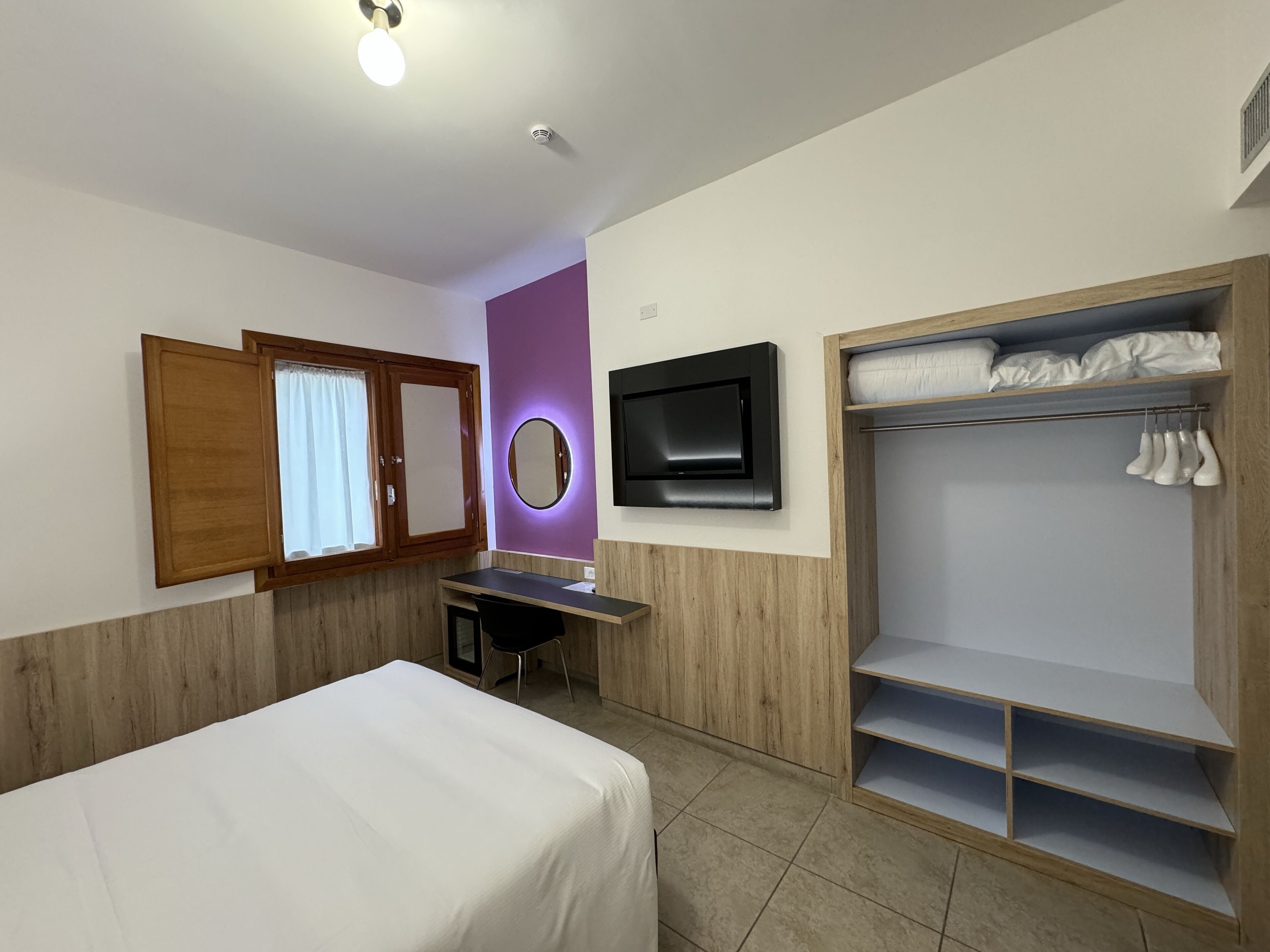 Una habitación de hotel con cama, escritorio, televisor, armario y espejo.