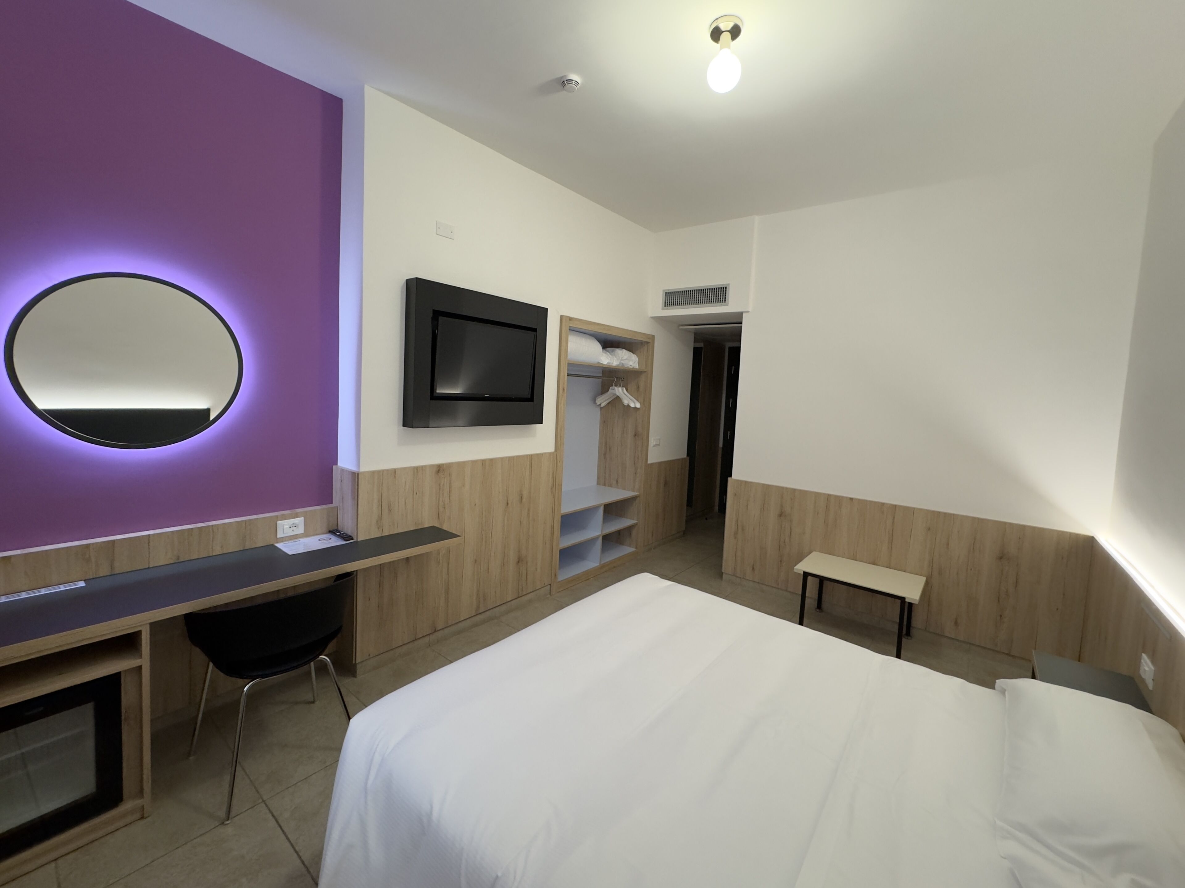 Una moderna camera d'albergo con un letto, una scrivania, una sedia, una televisione e un armadio.