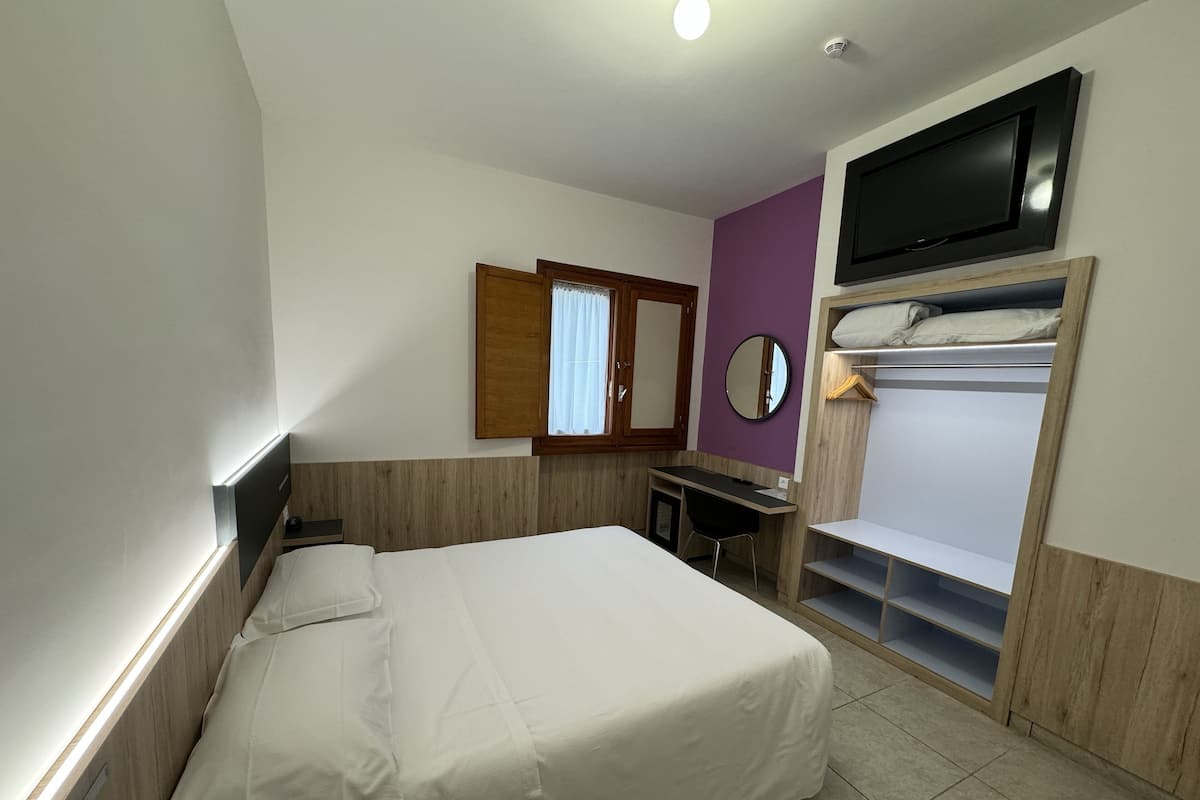 A hotel room with a bed, a desk, a wardrobe, and a TV.