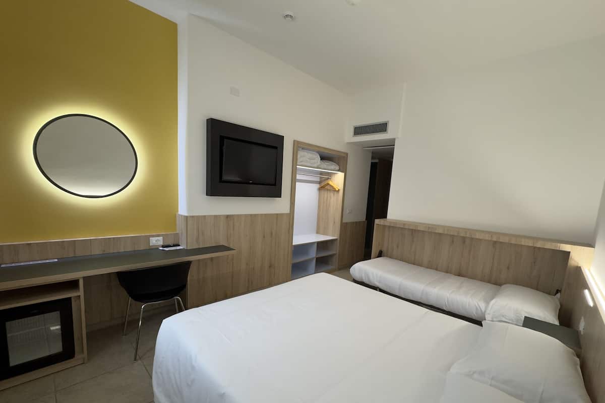 A hotel room with a bed, a desk, a chair, a TV, and a wardrobe.
