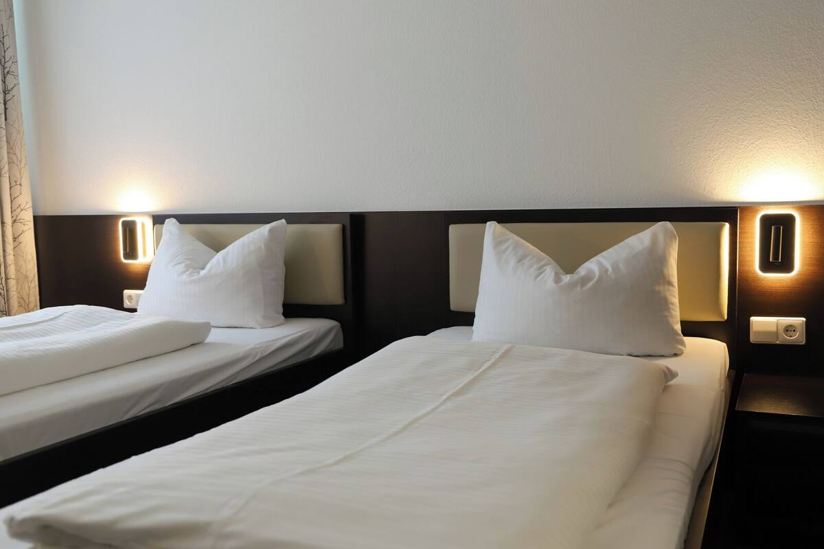 Two single beds with white linens and pillows, each with a headboard and bedside lamps.