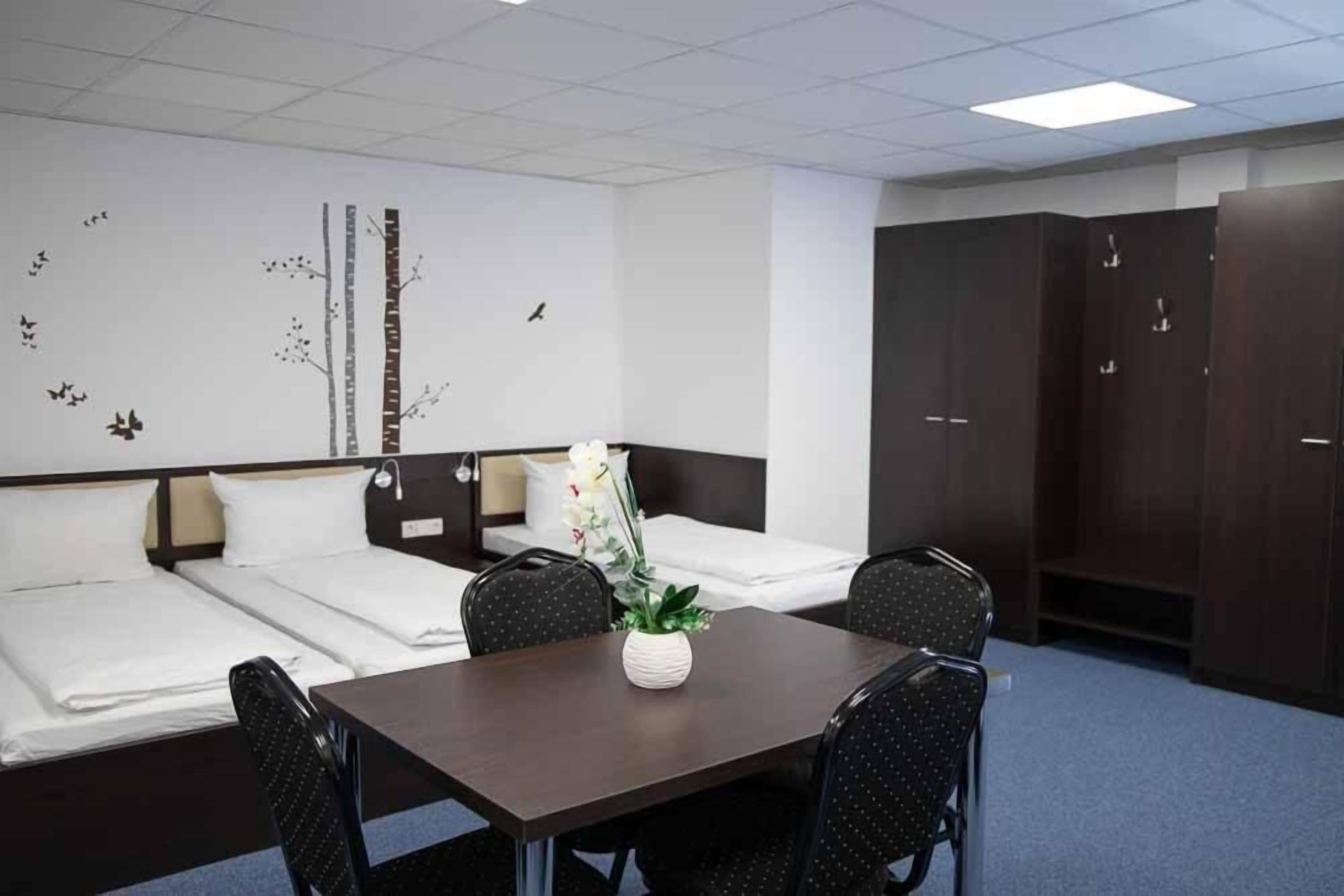 Habitación de hotel con dos camas, una mesa de comedor, sillas, un armario y una decoración de temática natural en la pared.