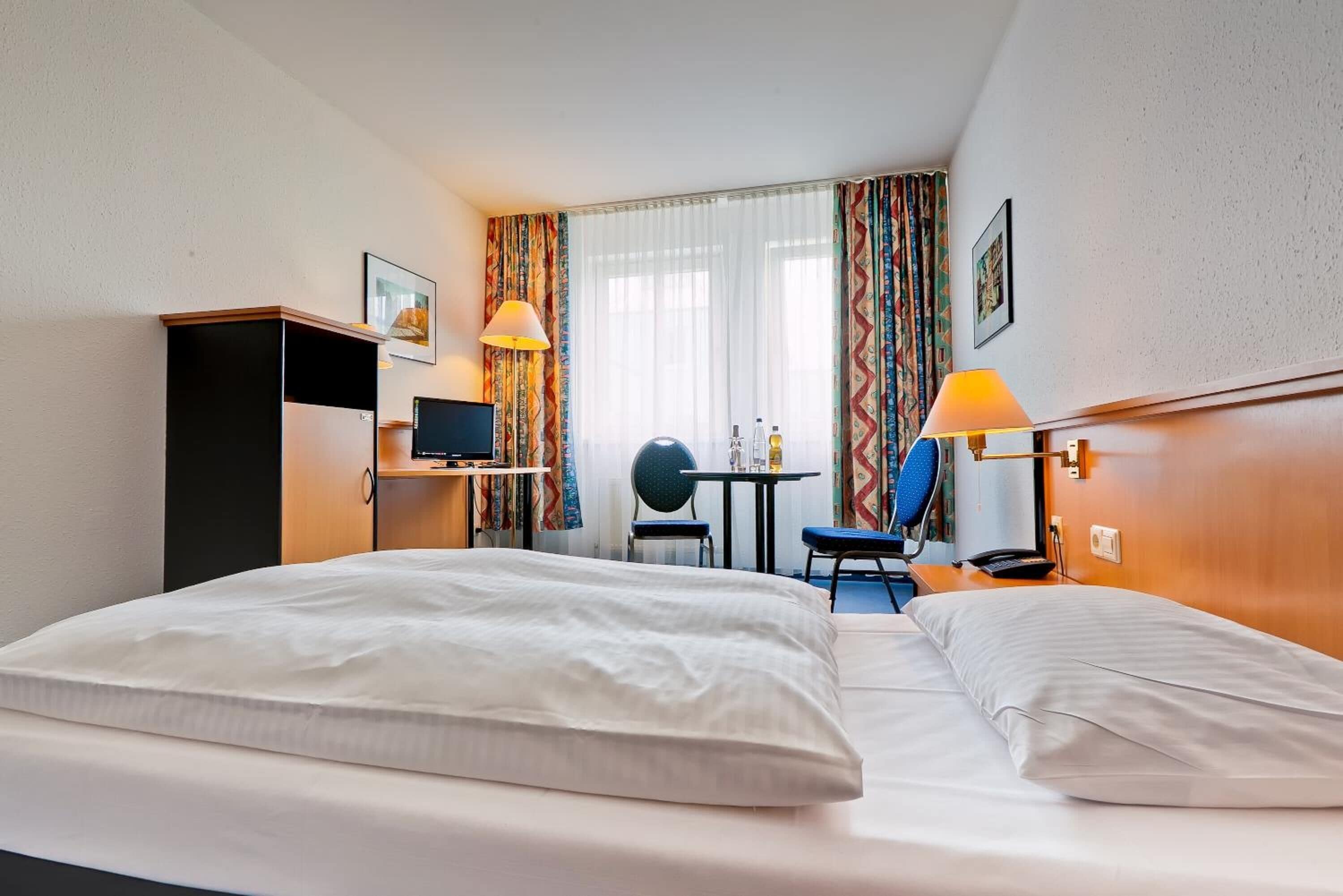 Habitación de hotel con dos camas, un escritorio, una silla, un televisor y una mesa con lámpara.
