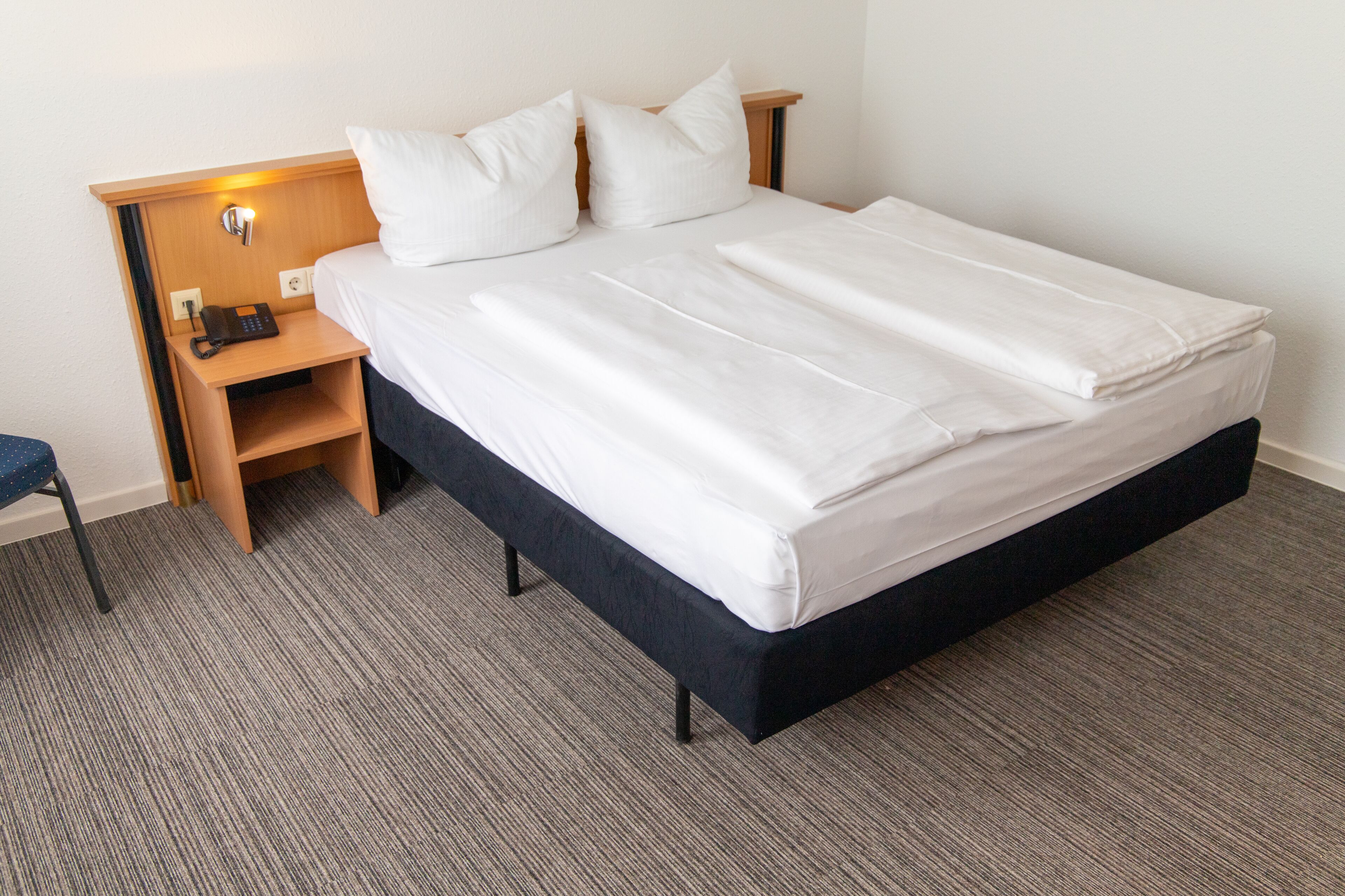 Una habitación de hotel con una cama grande, una mesita de noche con lámpara y un teléfono.