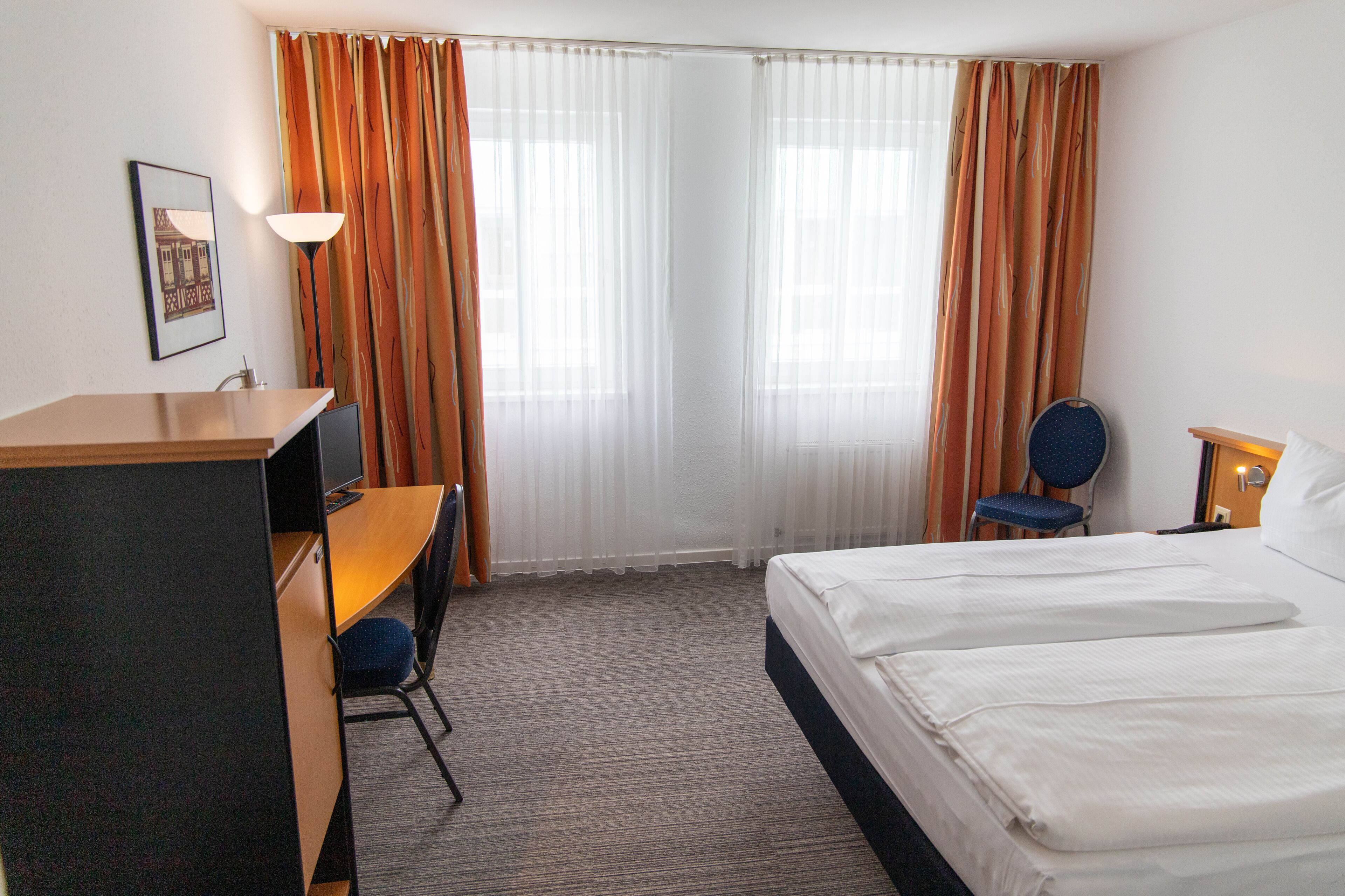 Habitación de hotel con cama, escritorio, silla y cortinas.