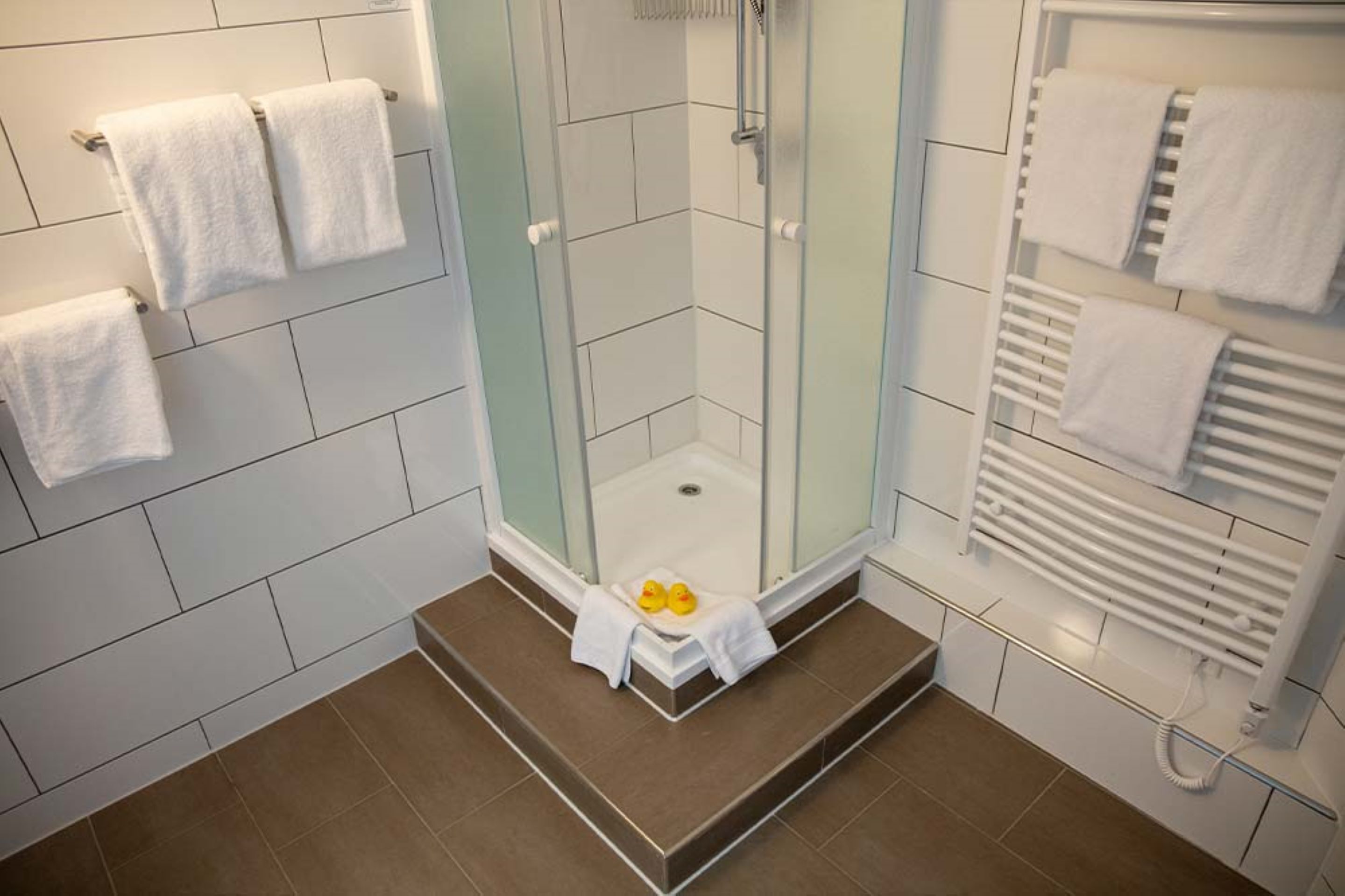 A modern bathroom with a glass-enclosed shower, white tiled walls, and a built-in towel rack.