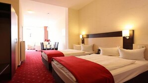 A hotel room with two beds, a red carpet, and a dining area in the background. - Adesso Hotel (Kassel)