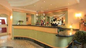 A reception area with a curved counter, a receptionist, and a mirror reflecting the interior. - Adesso Hotel (Kassel)