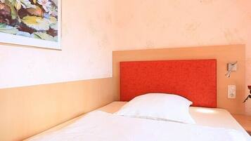 Una cama individual con cabecera roja en una habitación con pared texturizada y un cuadro enmarcado con motivos florales.
