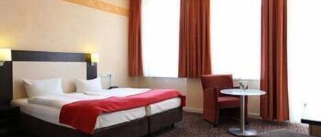 A hotel room with a bed, a chair, a small table, and a window with curtains.