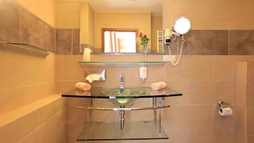 Un baño moderno con lavamanos de vidrio, un espejo, toallero y soporte para papel higiénico.