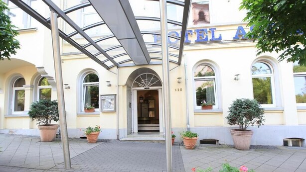 A hotel entrance with a covered walkway, potted plants, and a sign above the door. - Adesso Hotel (Kassel)