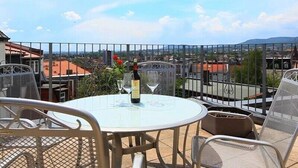 A round glass table with metal chairs, a bottle of wine, and a glass on it, set against a cityscape view. - Adesso Hotel (Kassel)