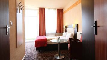 A hotel room with a bed, a small table, a chair, a nightstand, and a window with curtains.