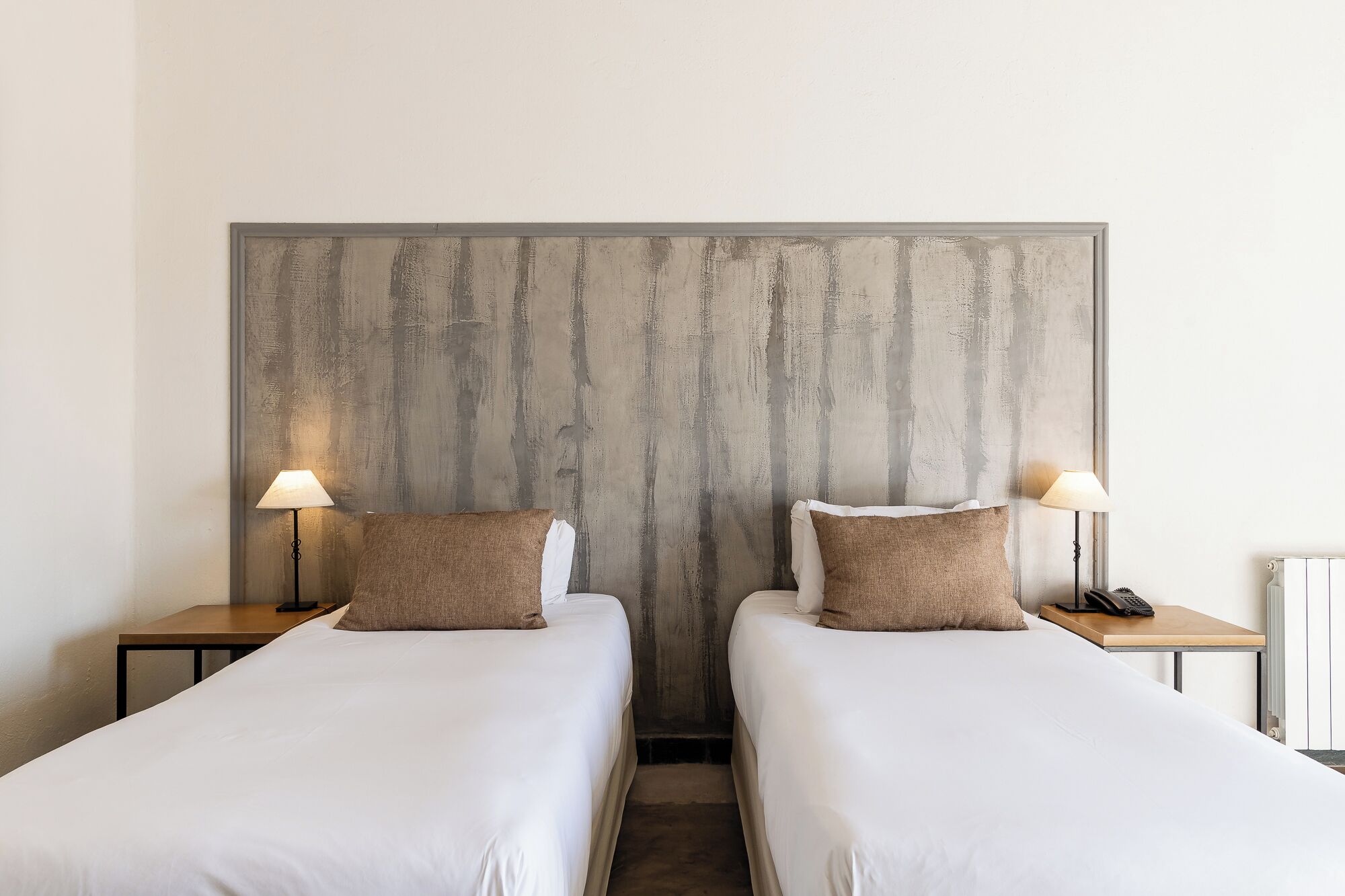 Una habitación de hotel con dos camas individuales, cada una con una almohada y una lámpara de noche.