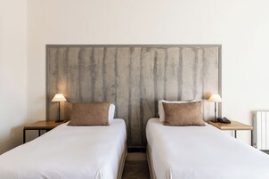 Una habitación de hotel con dos camas individuales, cada una con una almohada y una lámpara de noche.