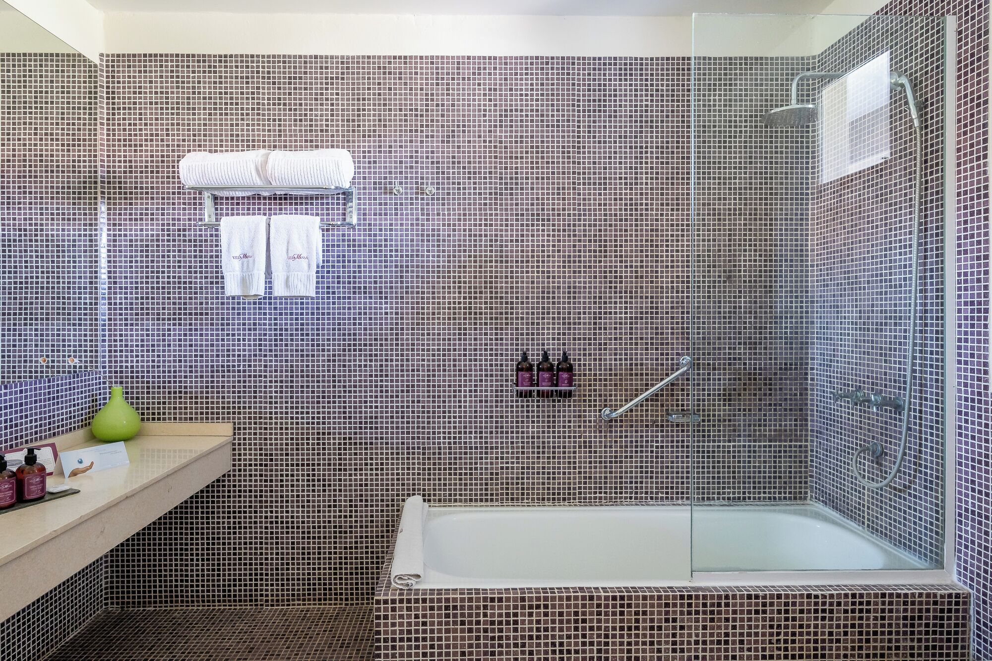 Un baño con pared de ducha azulejada, una bañera y un perchero con toallas.