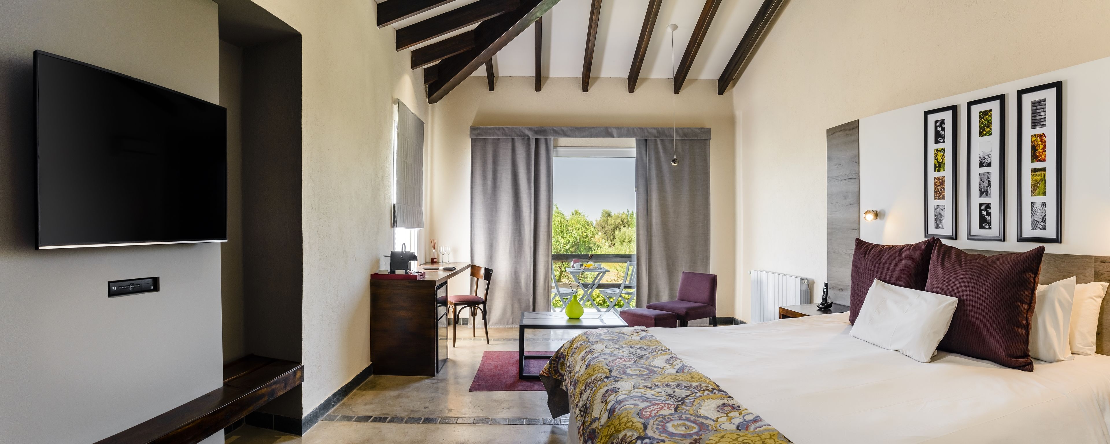Habitación de hotel con una cama grande, un televisor montado en la pared, un escritorio con una silla y un balcón con vistas a zonas verdes.