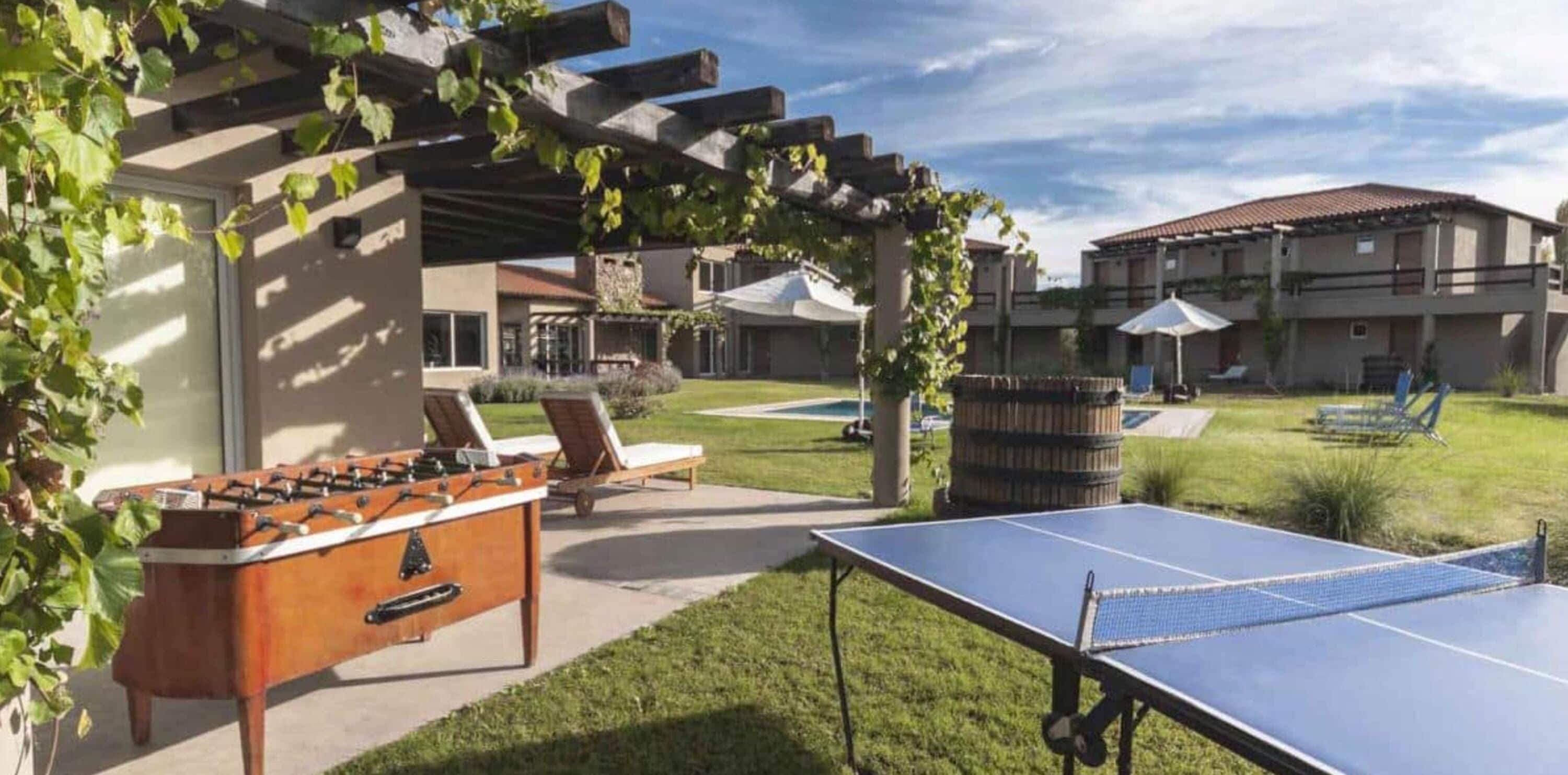 An outdoor recreational area with a foosball table, a ping pong table, and lounge chairs.
