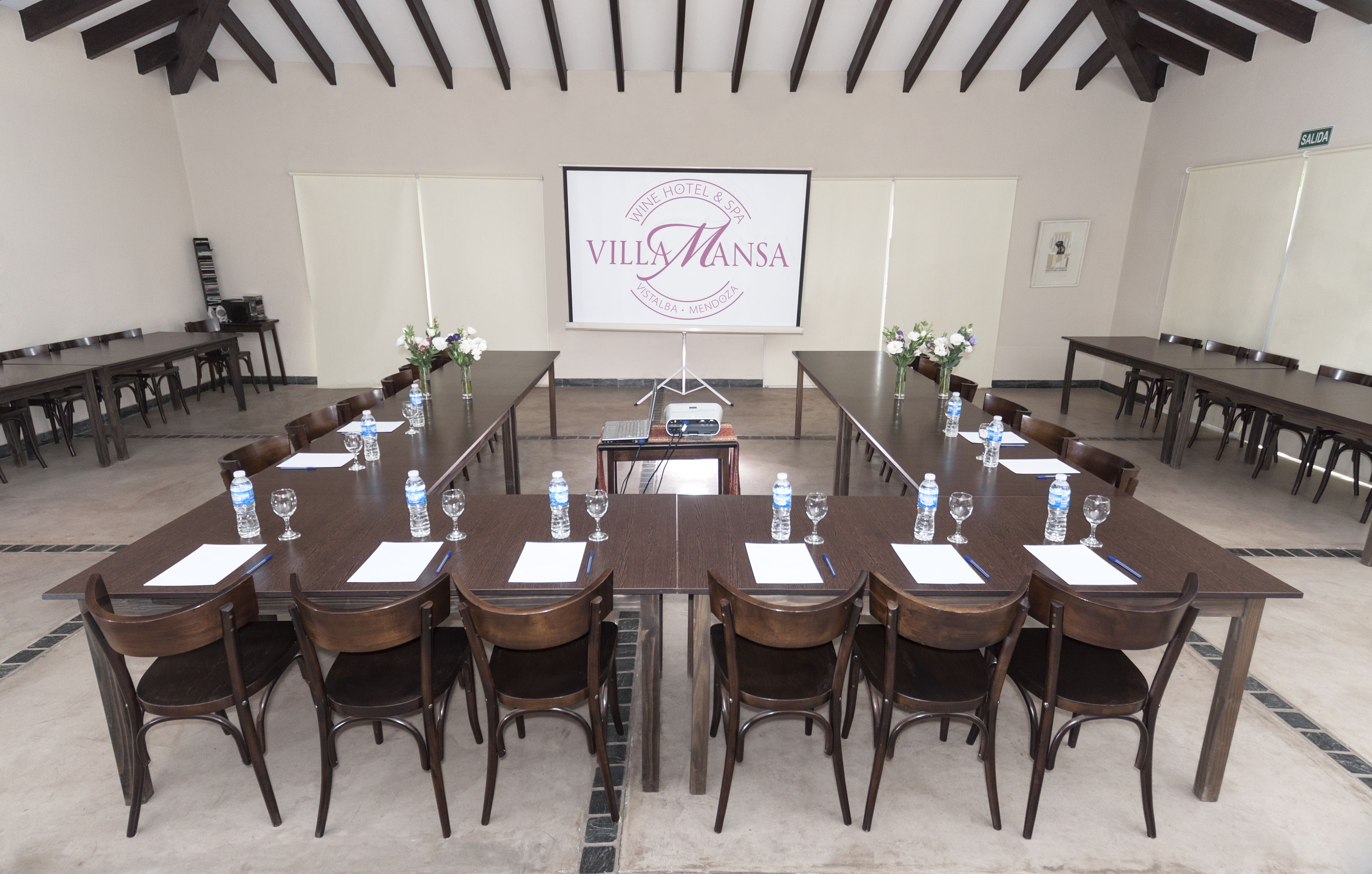 Un salón de conferencias con una larga mesa, sillas, botellas de agua y una pantalla proyectora mostrando 