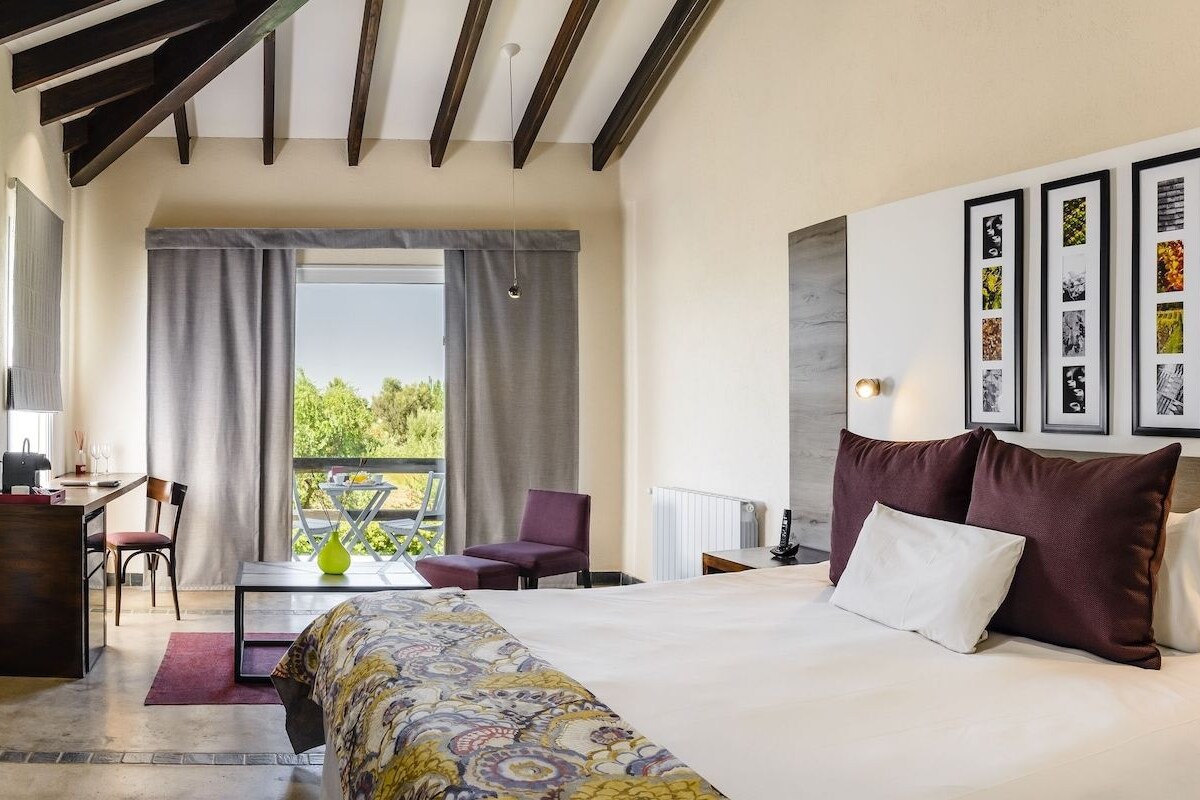 A hotel room with a bed, a desk, a chair, a TV, and a balcony with a view.