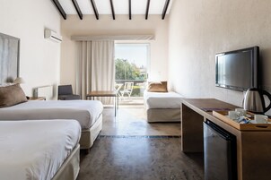 A hotel room with two beds, a desk, a television, and a balcony with a view.