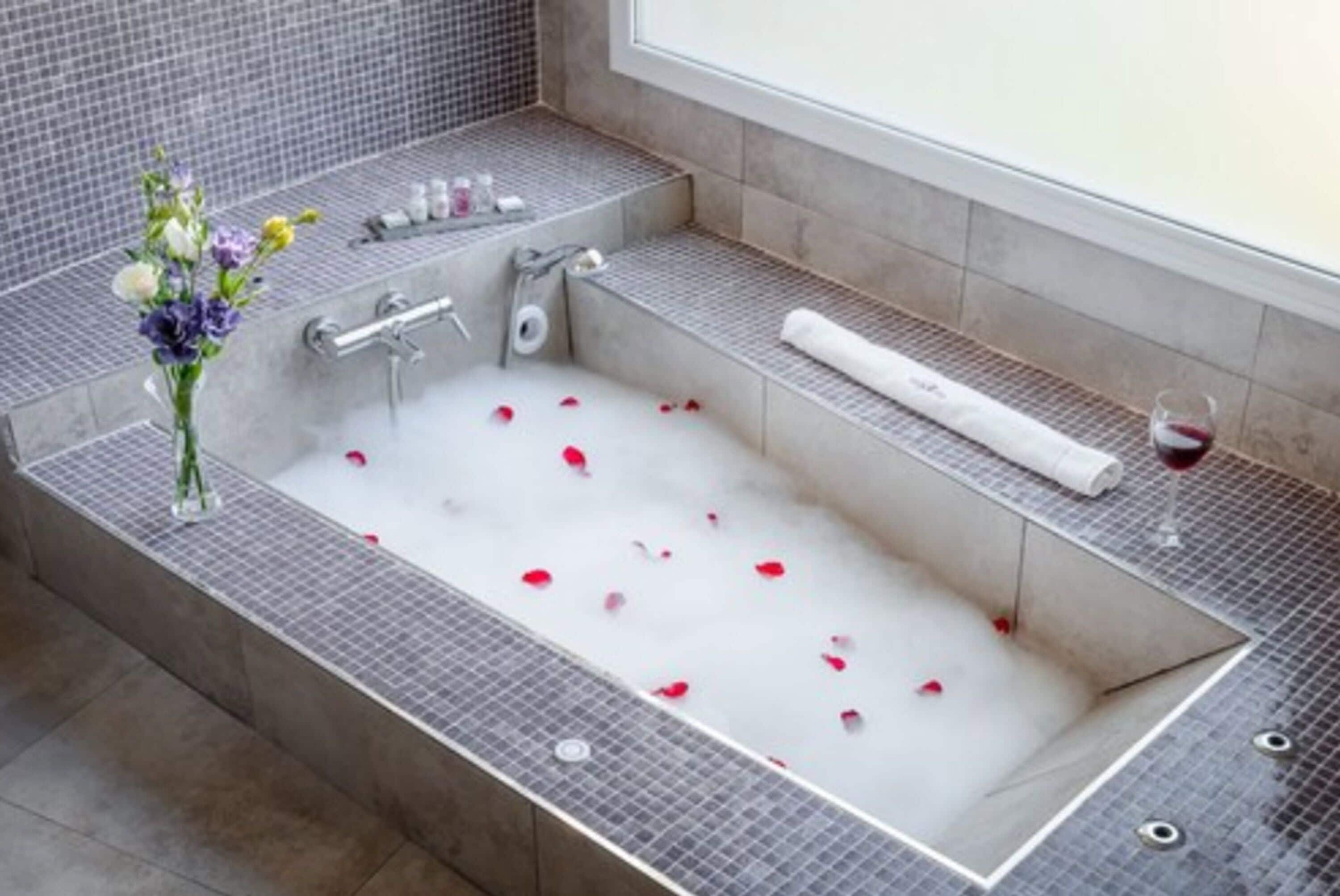 A modern bathroom with a large bathtub, a glass of red wine, and a vase of flowers.