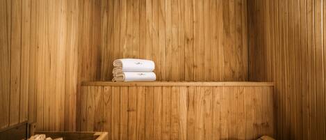 A wooden sauna with benches and a shelf holding towels.