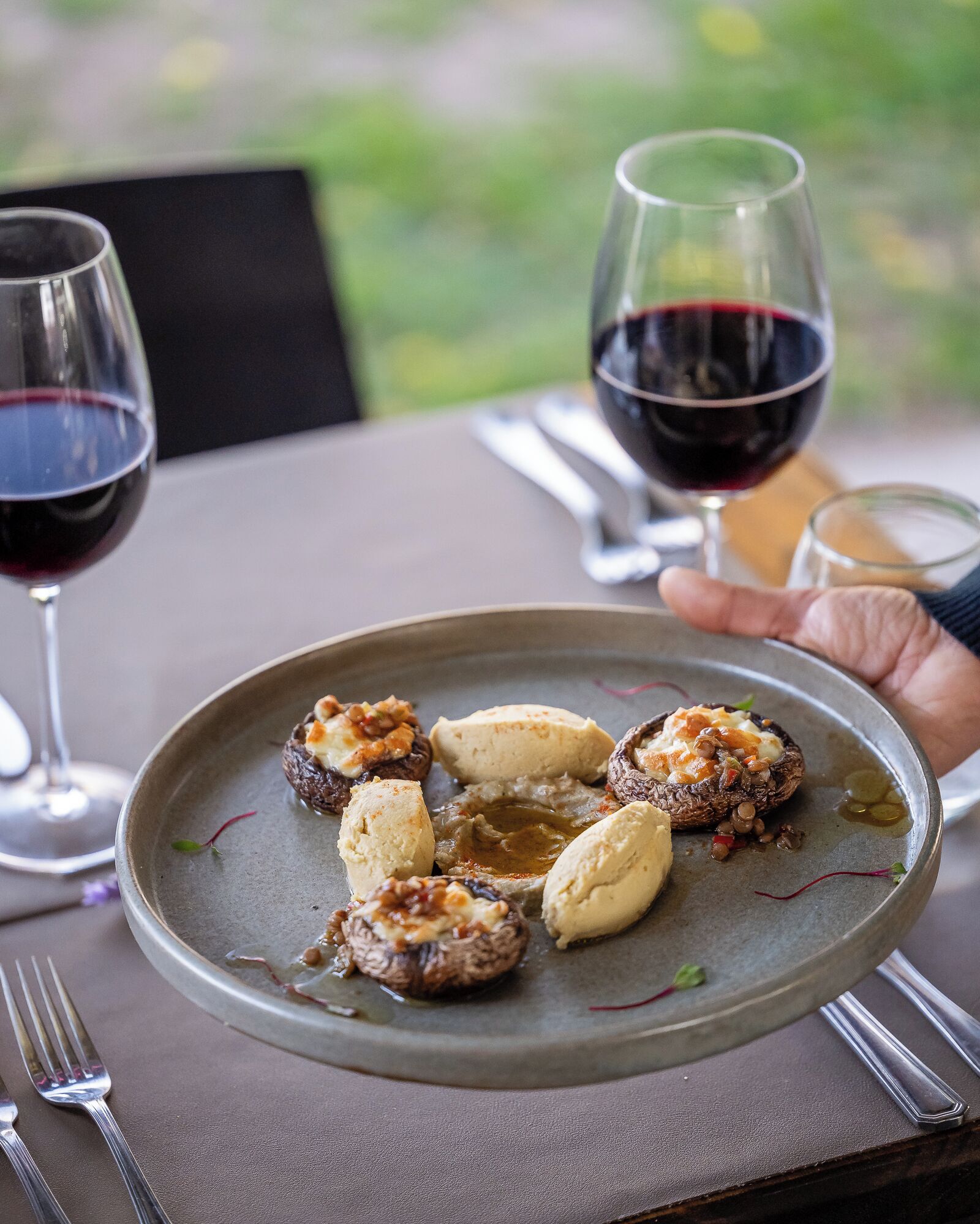 A plate of stuffed mushrooms with a side of sauce, accompanied by a glass of red wine and a small glass of water on a table.