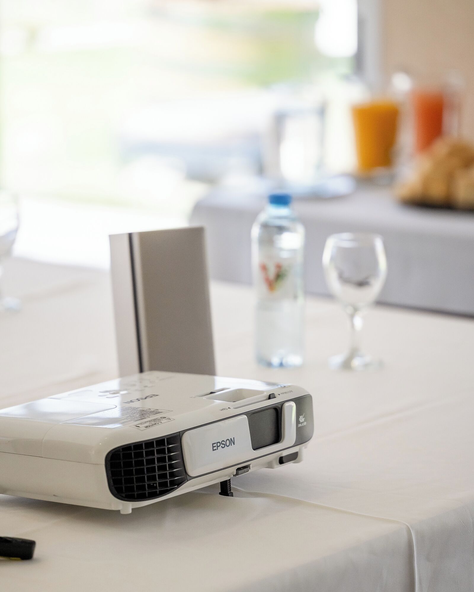 A projector on a table with a bottle of water and a glass in the background.