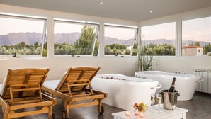 A spa room with two wooden loungers, a large bathtub, and a table with a bottle of champagne and glasses. - Villa Mansa Wine Hotel (Luján de Cuyo)