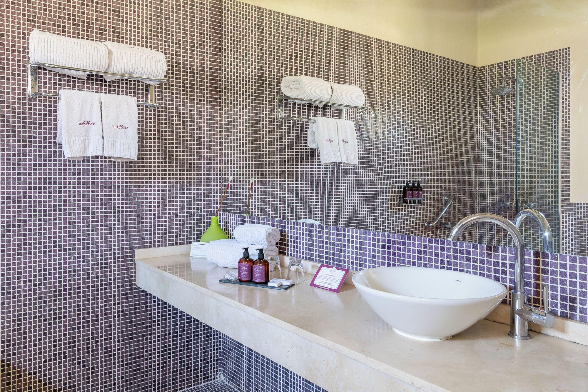 A bathroom with a tiled wall, a sink with a bowl, a mirror, and two towel racks with towels.