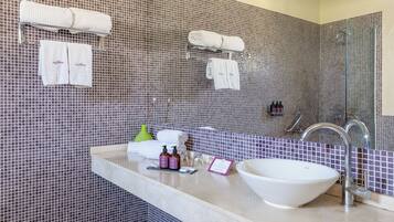 A bathroom with a tiled wall, a sink with a bowl, a mirror, and two towel racks with towels.