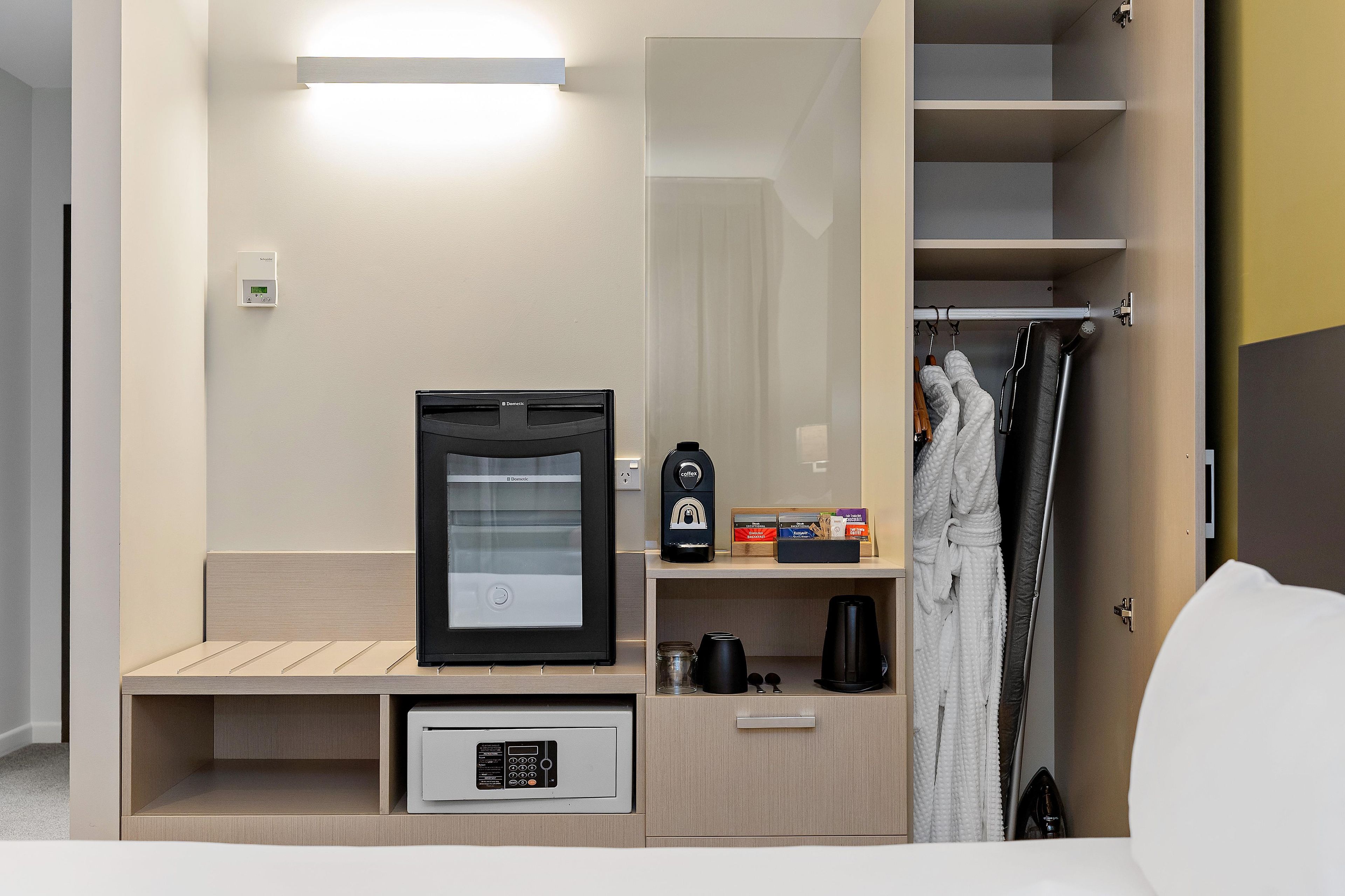 Habitación de hotel con minibar, cafetera, espejo y zona de ducha.