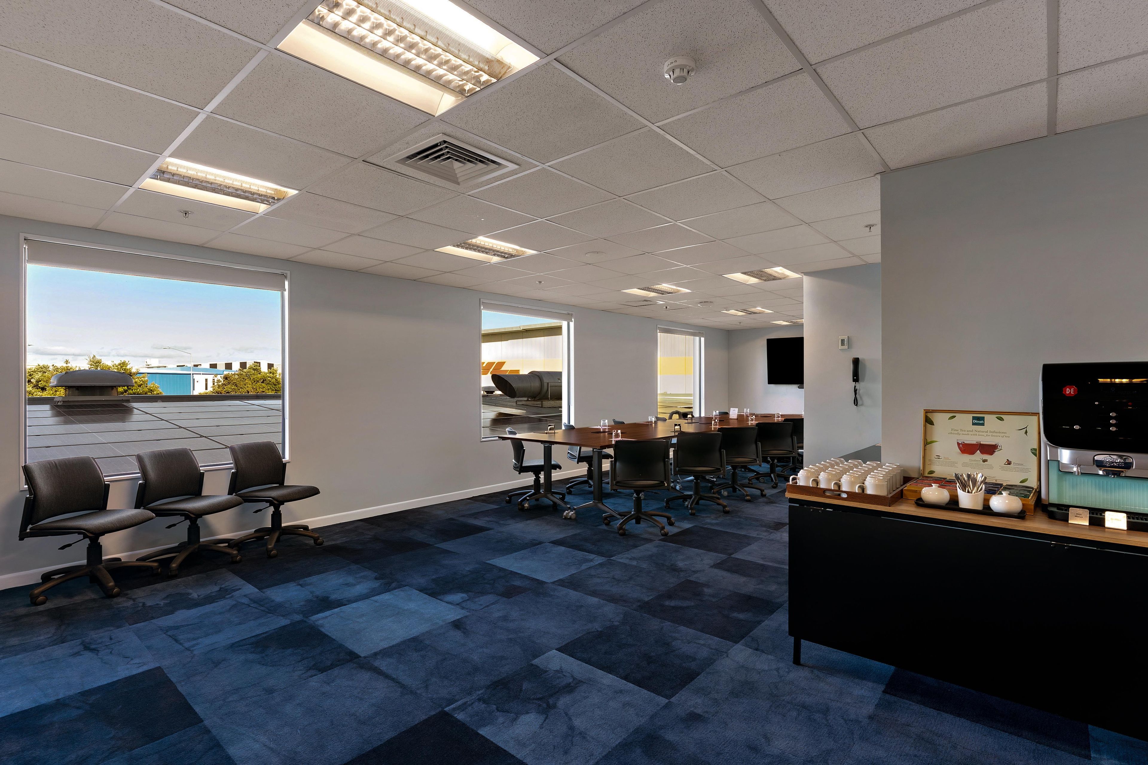 A conference room with a large table, chairs, a coffee station, and a view of the outdoors.