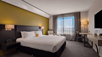 A hotel room with a large bed, a desk, a chair, and a view of the outdoors.