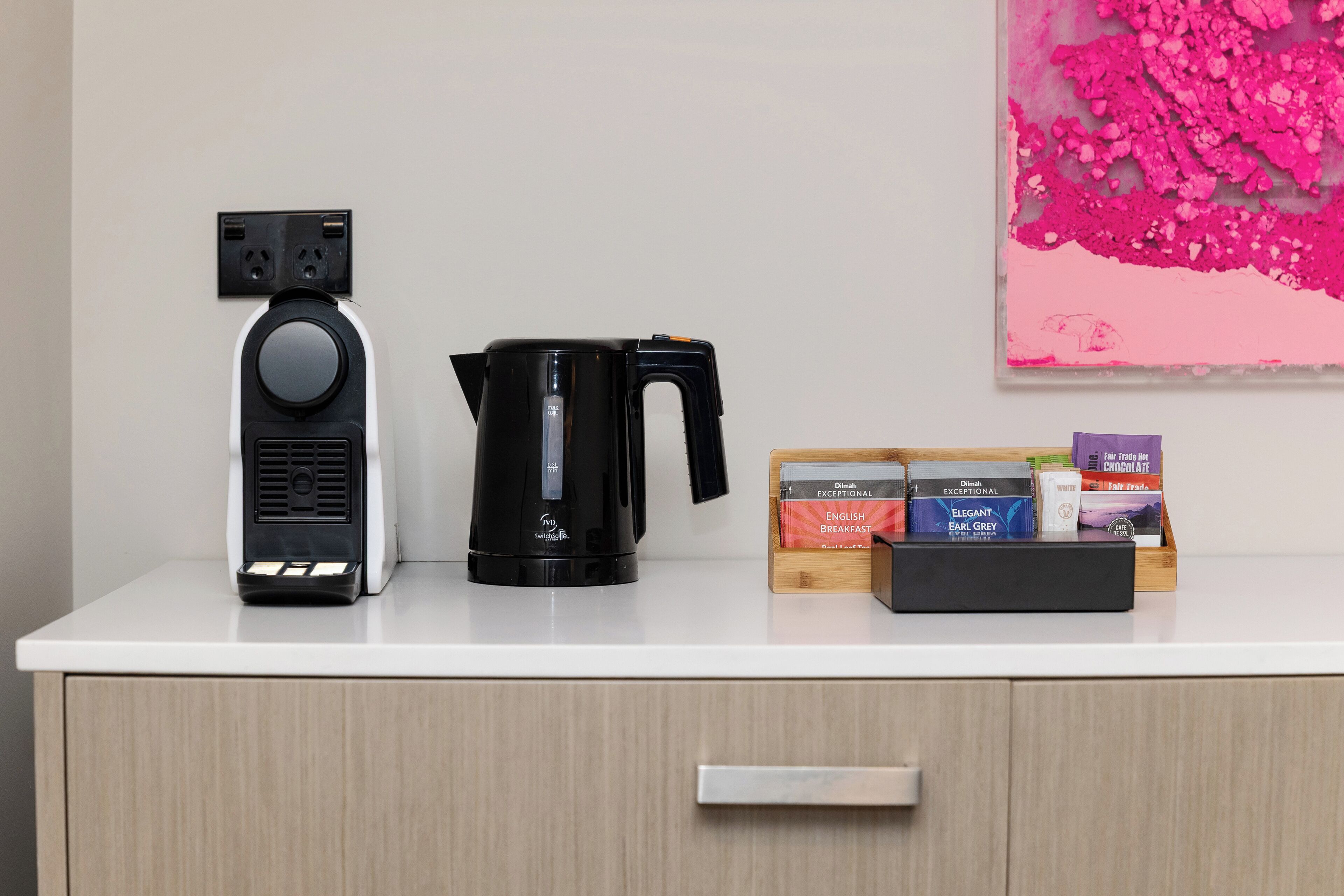 Una cafetera, un hervidor y una caja de bolsitas de té sobre una encimera blanca.